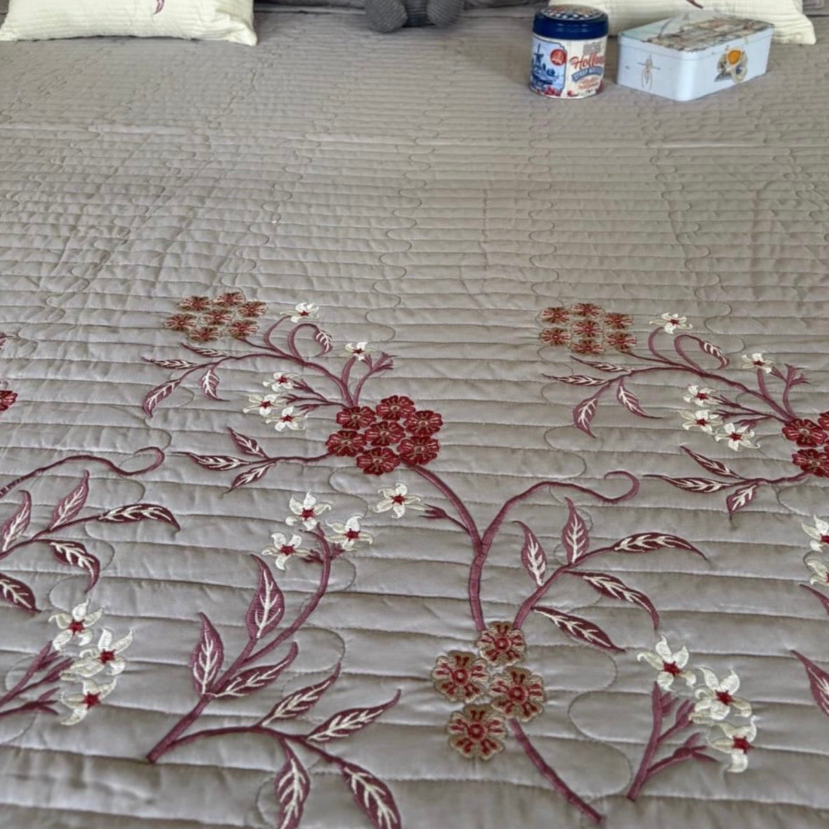 Embroidered bedspread with floral patterns on a bed with decorative pillows and a plush toy.