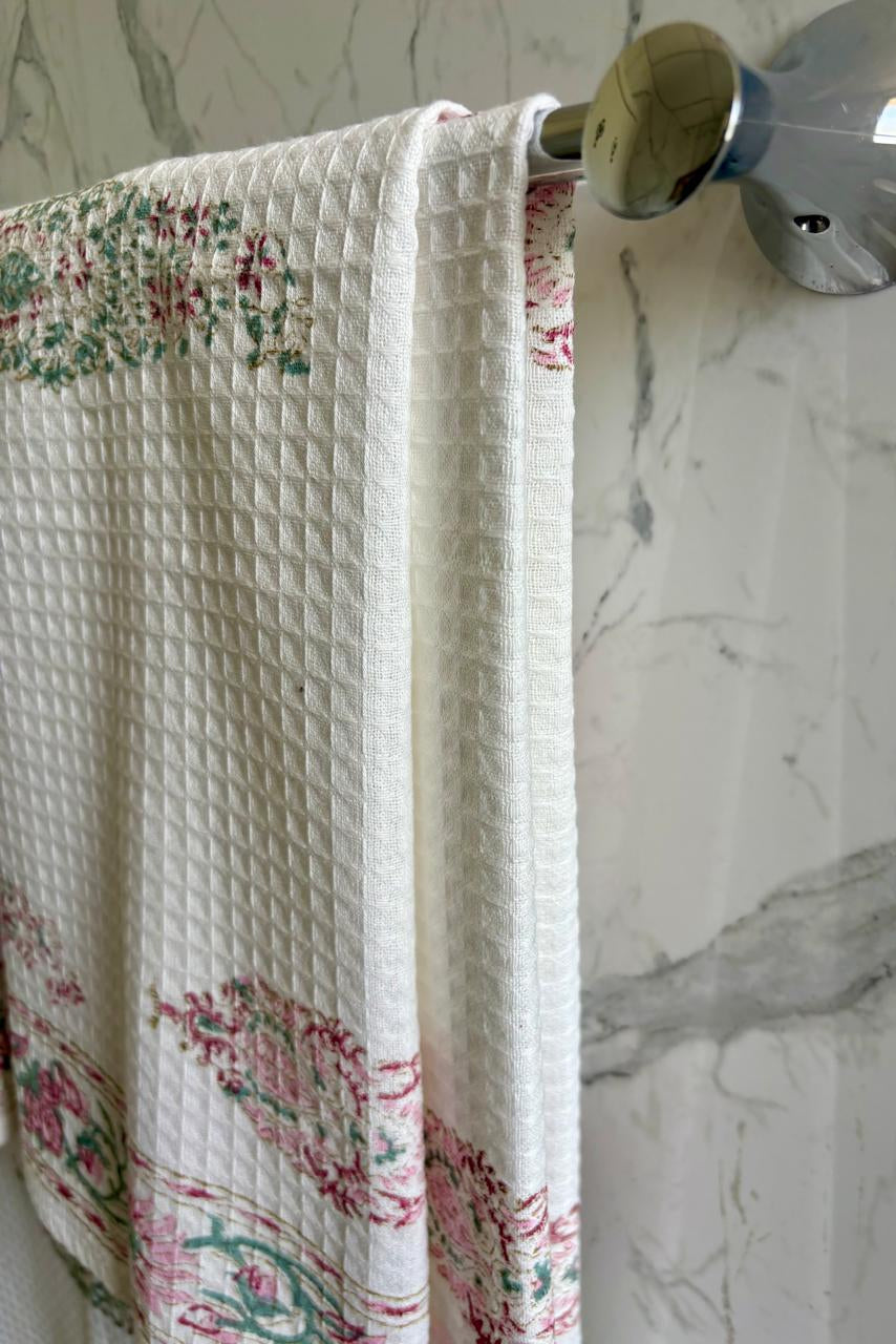 Floral-patterned towel hanging on a silver towel rack against a marble wall.