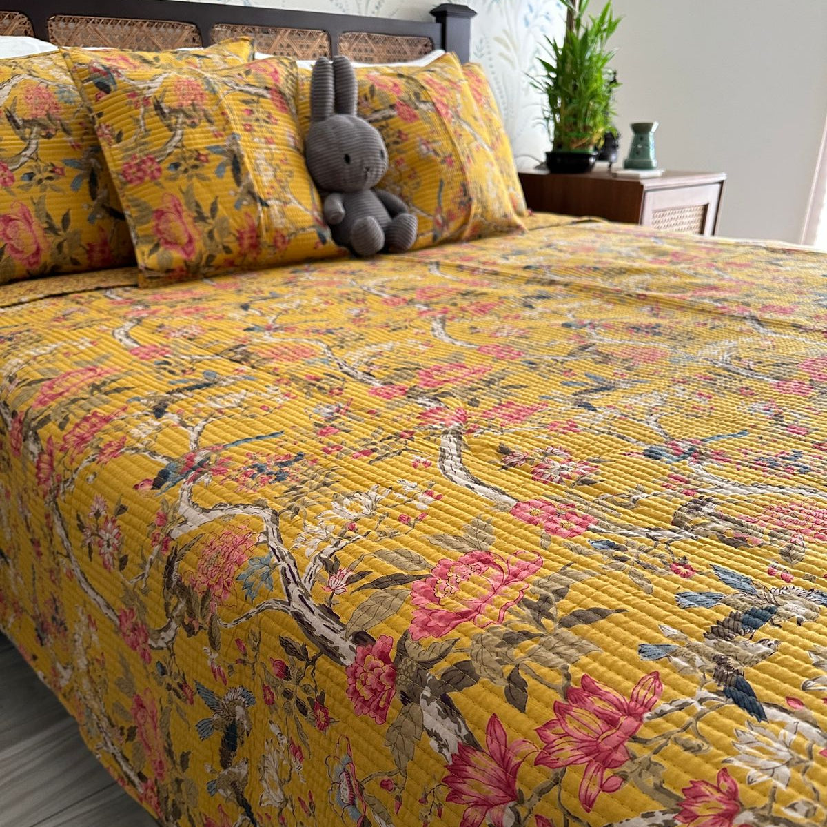 Yellow floral quilt on a bed with a gray stuffed animal, in a bedroom setting.