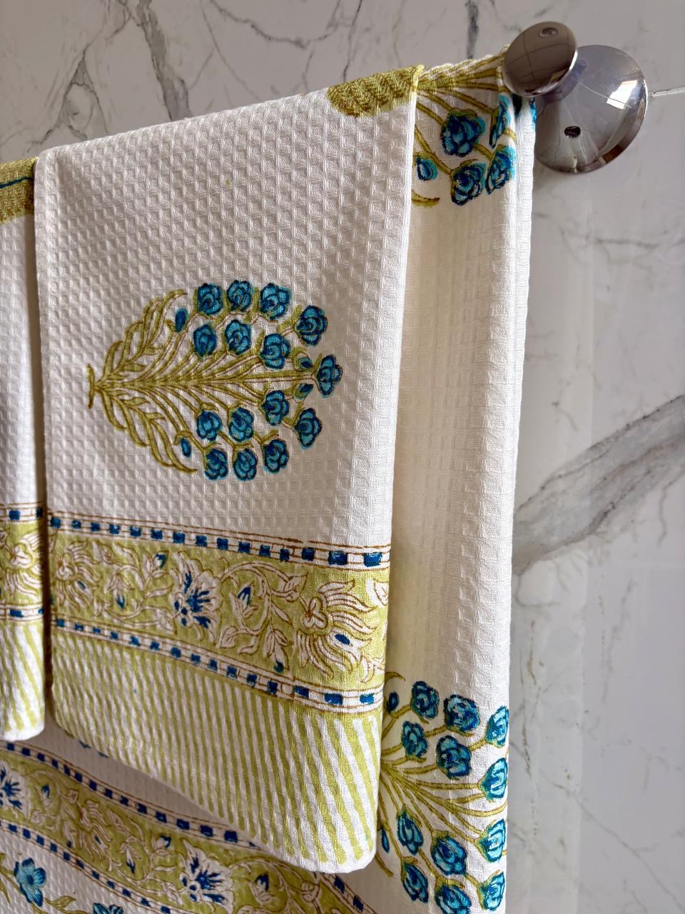 Decorative towel with peacock design hanging on a towel rack against a marble wall.