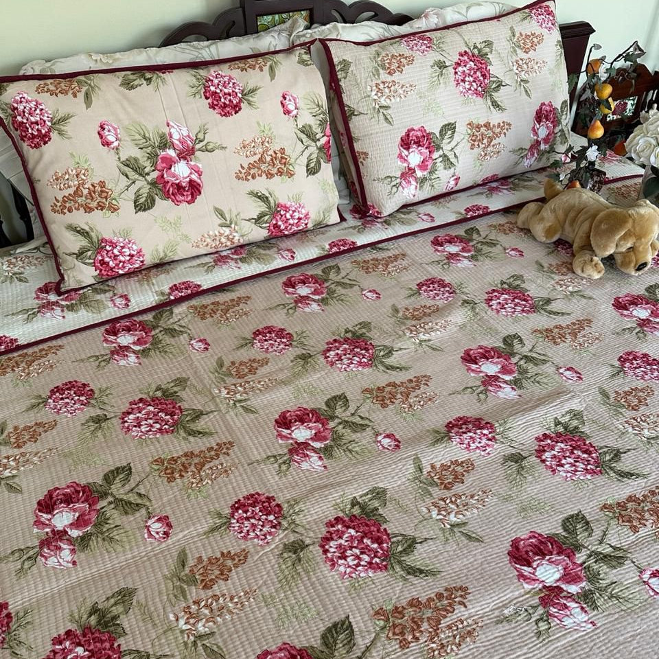 Floral patterned bedspread with matching pillows on a bed.