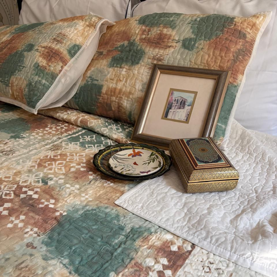 Quilt with geometric patterns on a bed with decorative items.