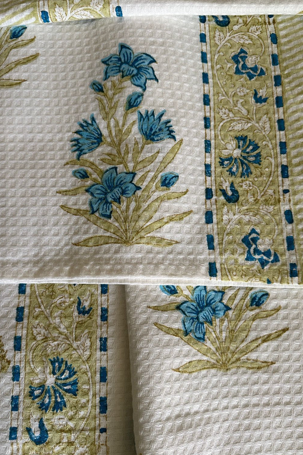 Close-up of a quilt with floral patterns in blue and green on a beige background.