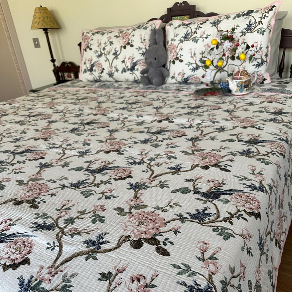 Floral and bird patterned quilt on a bed with matching pillows.