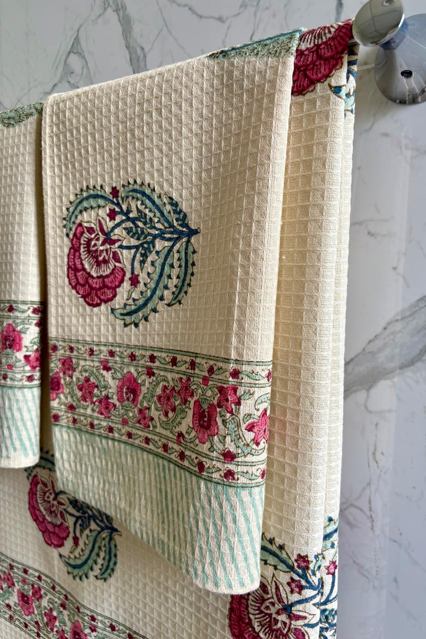 Decorative towel with floral patterns hanging on a rack against a marble wall.