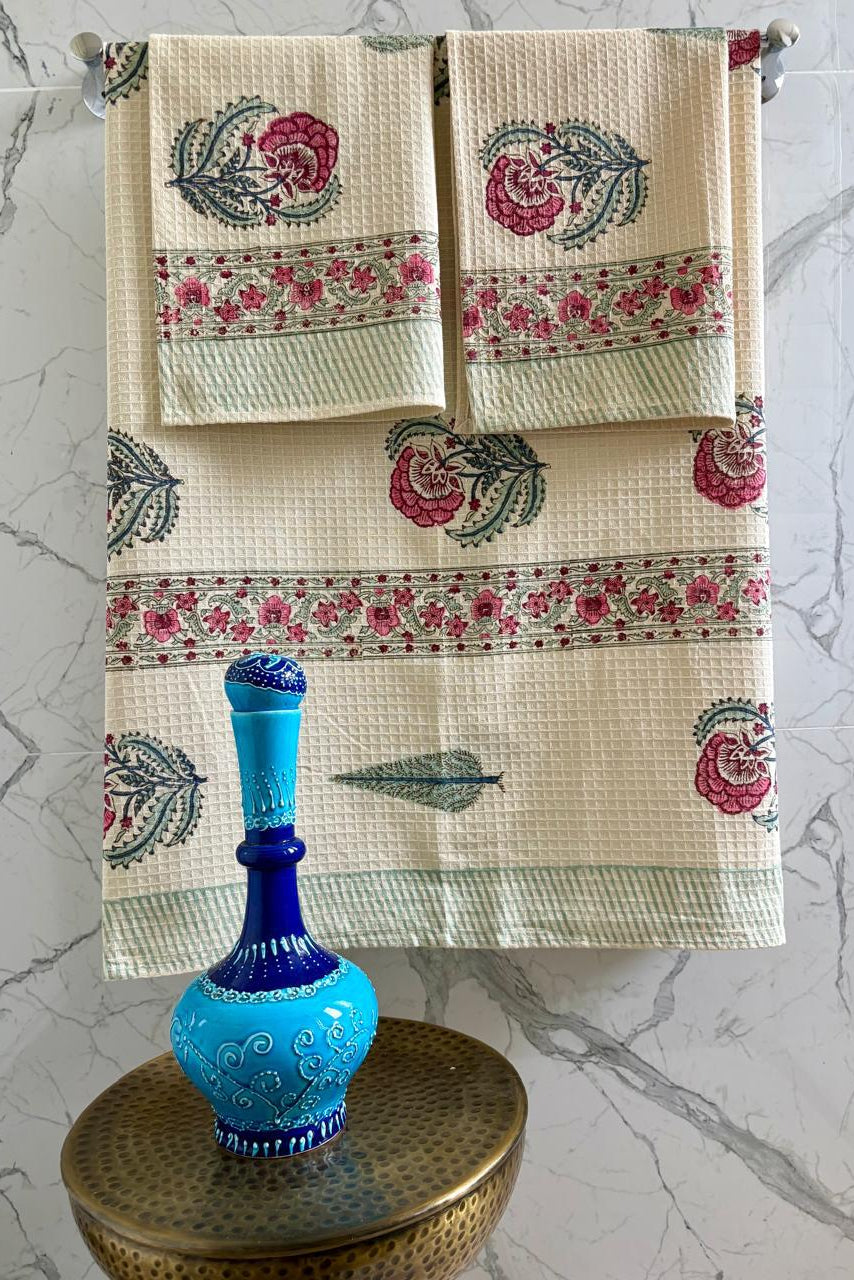 Decorative towels with floral patterns hanging on a rack against a marble wall.