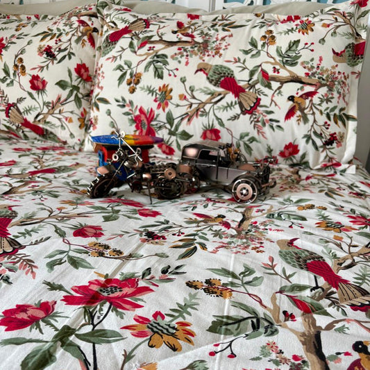Floral and nature-themed bedspread with decorative pillows and a toy train on a bed.