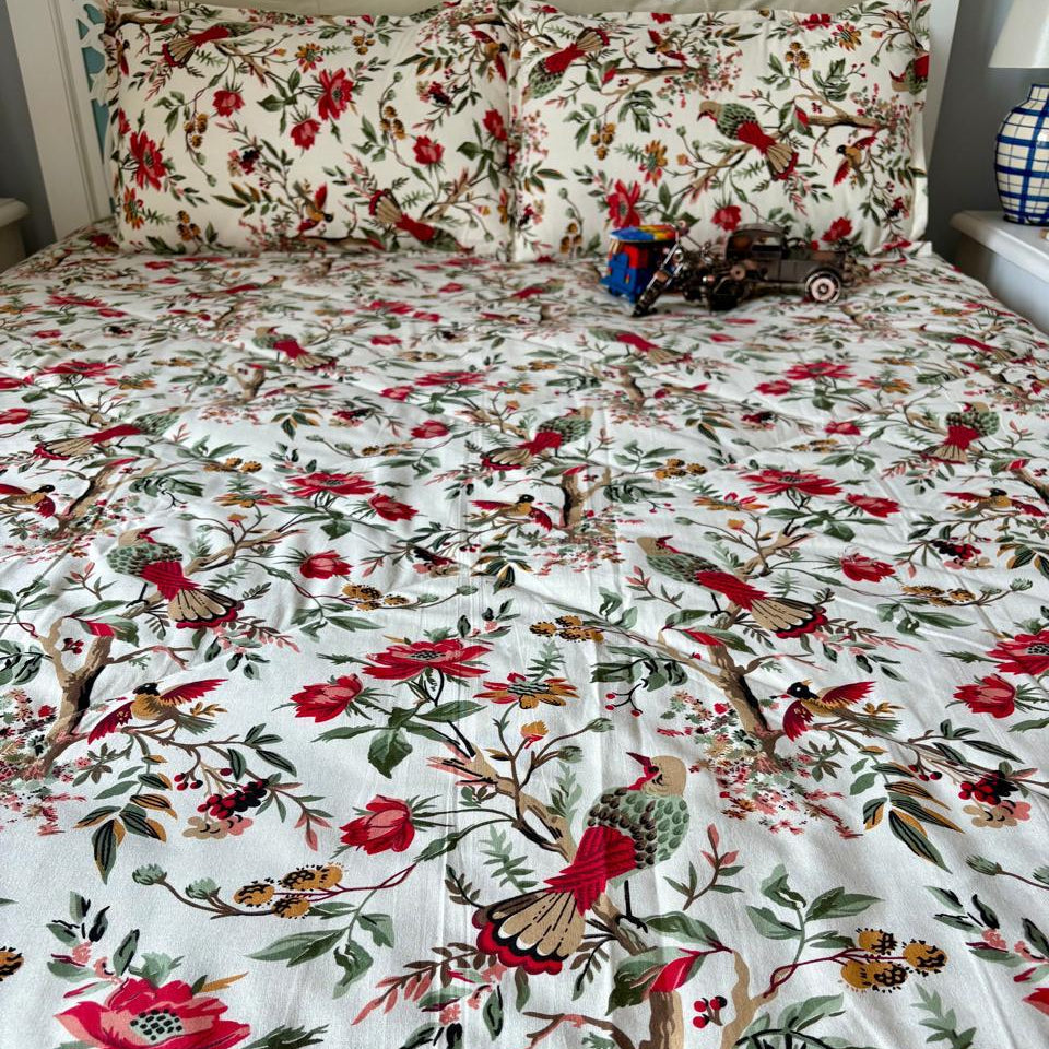Floral and bird patterned bedspread on a bed with pillows.