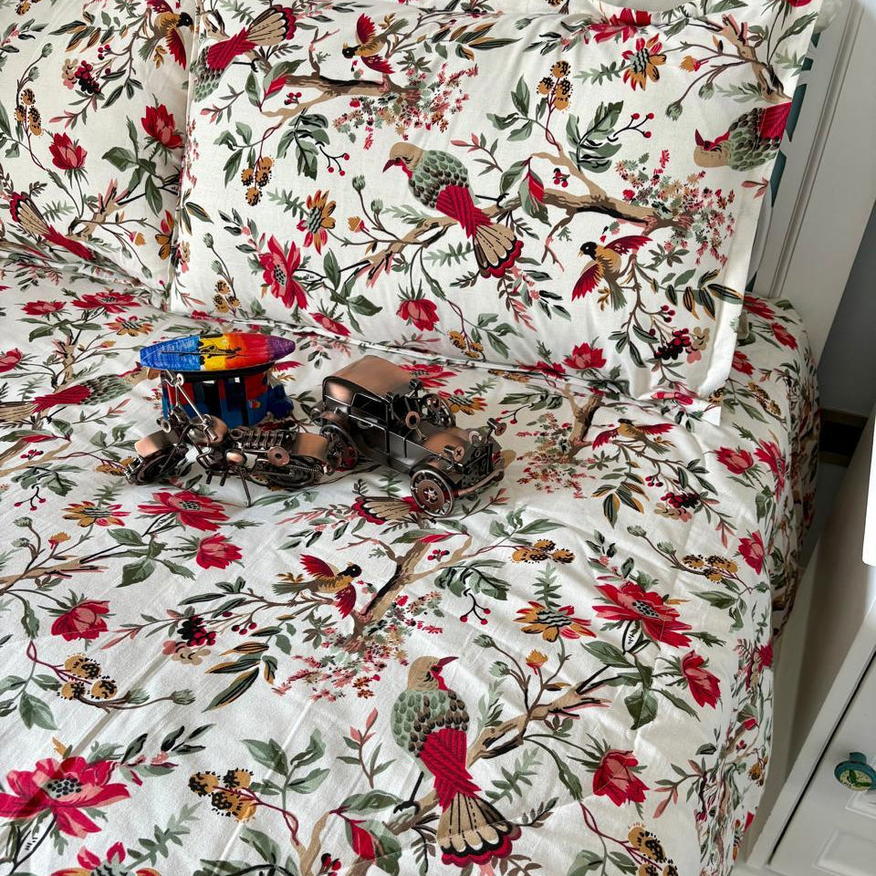 Floral and bird patterned bedspread on a bed with a white nightstand.