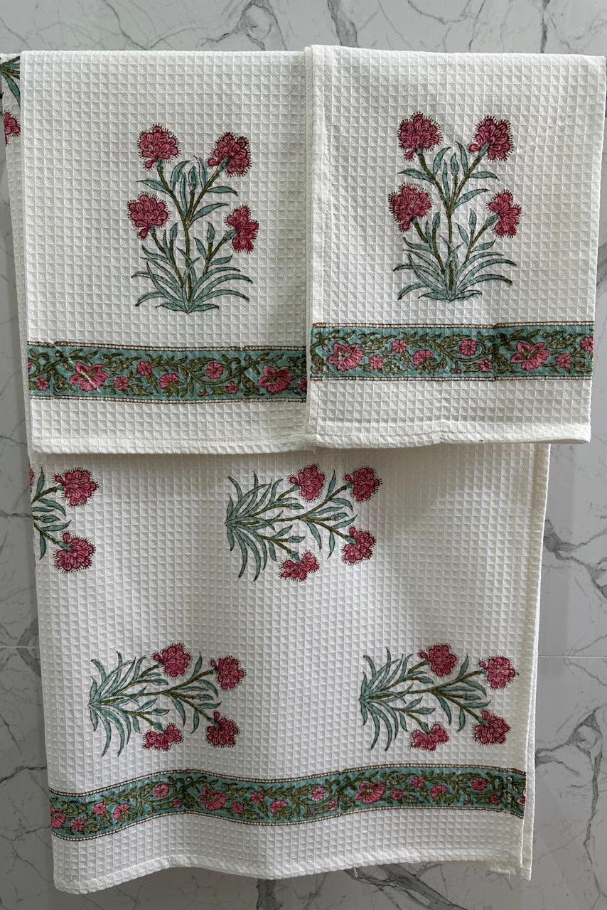 Set of three white towels with floral embroidery on a gray marble background