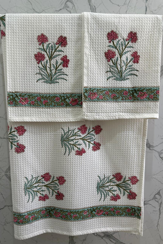 Set of three white towels with floral embroidery on a gray marble background