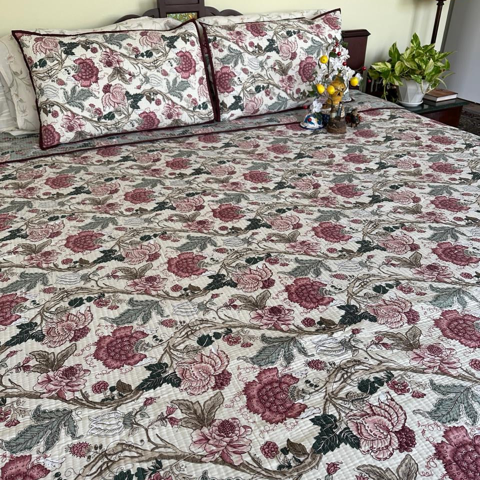Floral patterned bedspread on a bed with pillows and a lamp in the background.