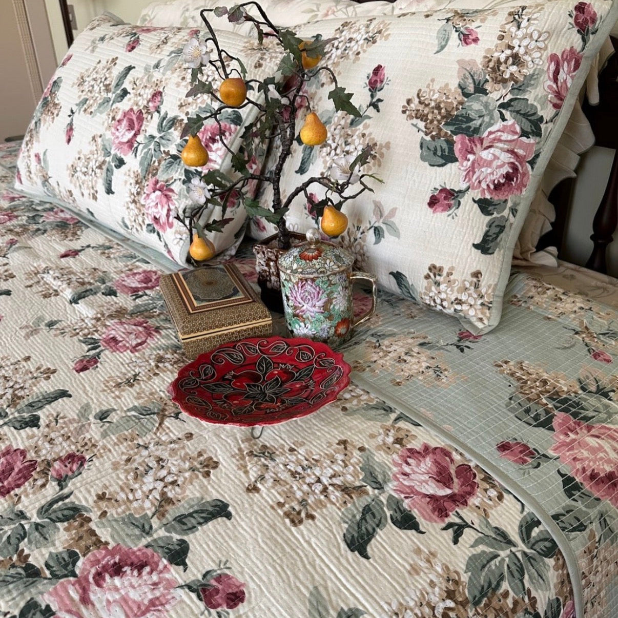 Floral-patterned bedspread with decorative pillows and a small tree on a bed.