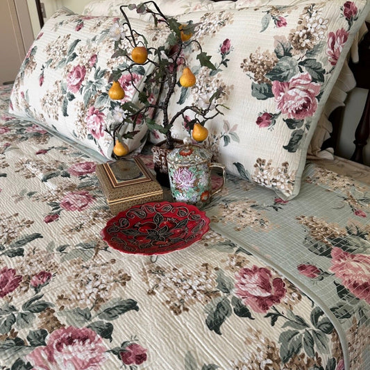 Floral-patterned bedspread with decorative pillows and a small tree on a bed.