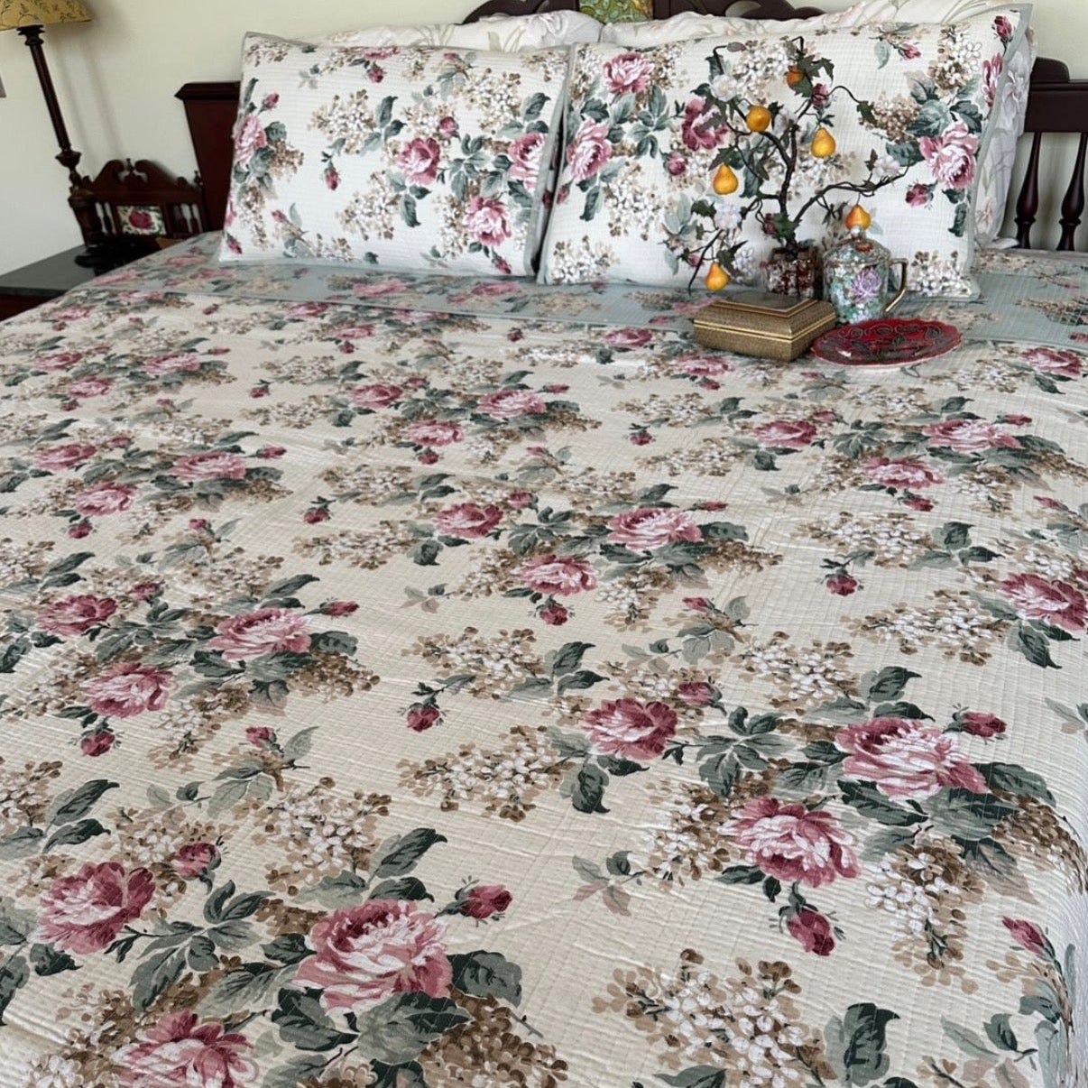 Floral quilt and pillow set on a bed with a lamp and decorative items in the background.