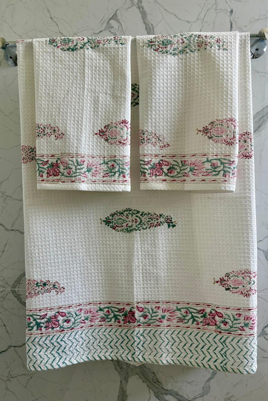 Decorative towels with floral patterns hanging on a towel rack against a marble background.