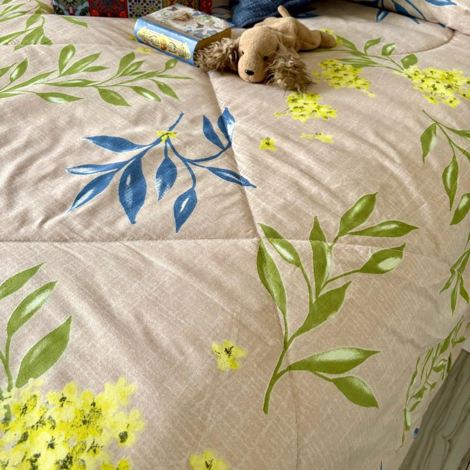 Floral-patterned comforter on a bed with a teddy bear and tissues.