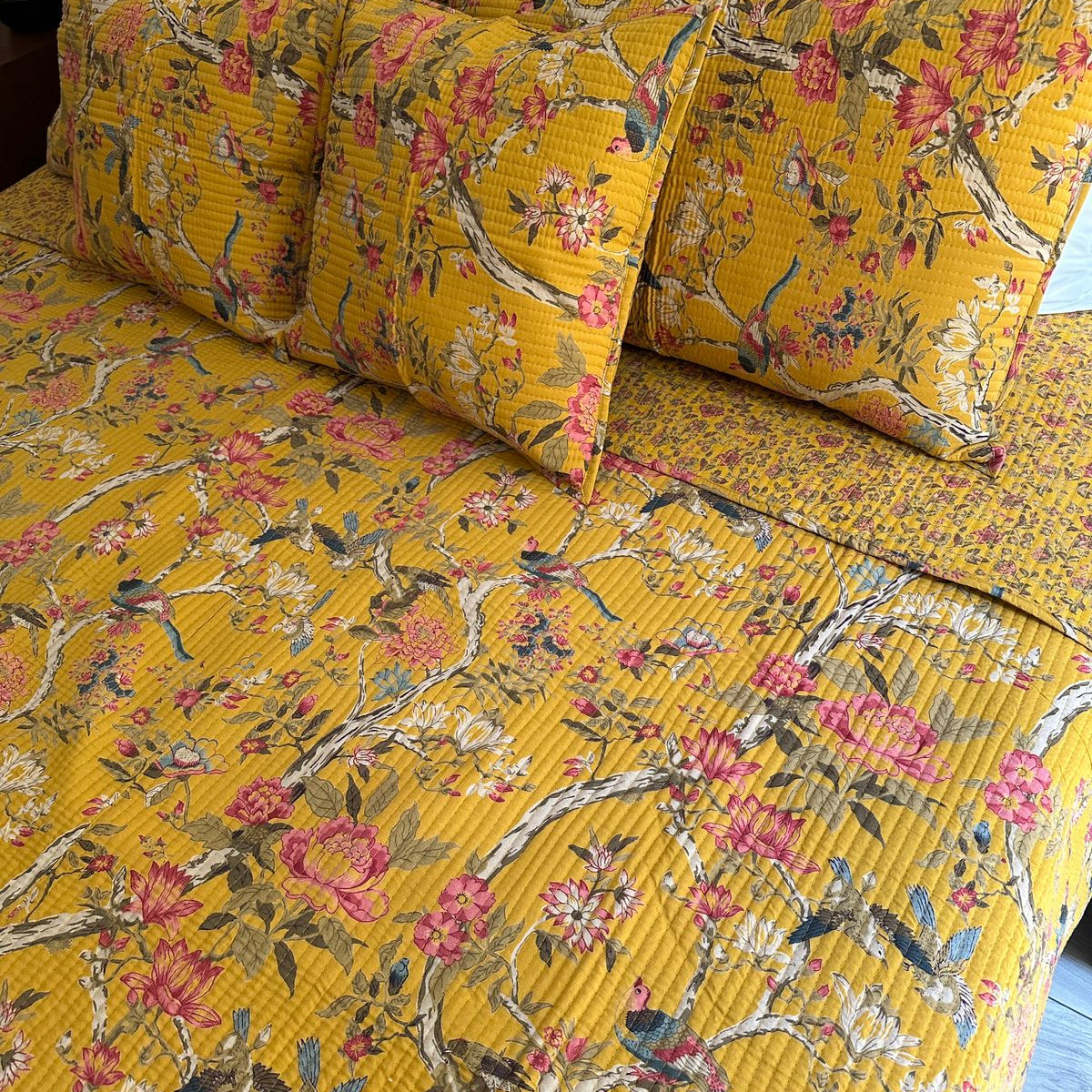 Yellow floral and bird patterned bedding set on a bed.