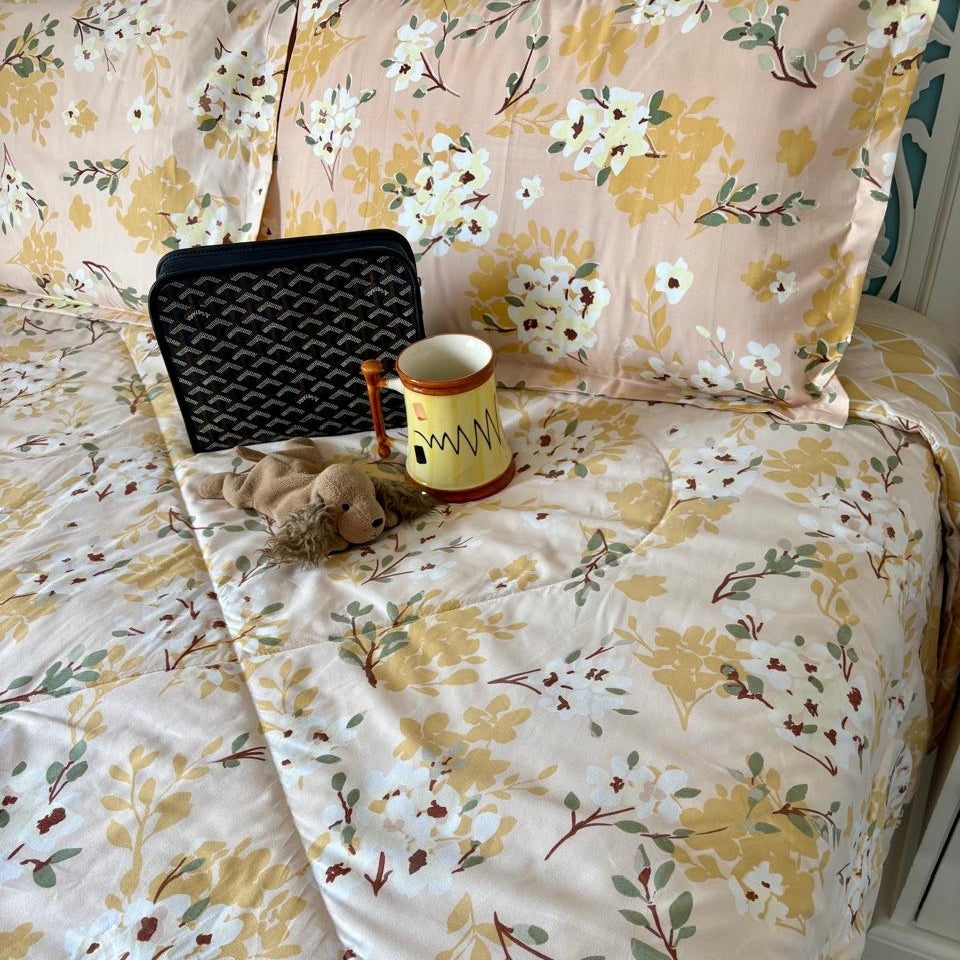 Floral-patterned bedding with a teddy bear, mug, and black bag on a bed.
