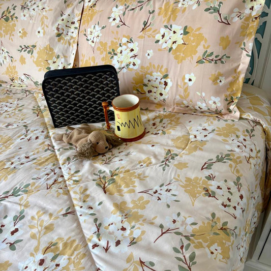 Floral-patterned bedding with a teddy bear, mug, and black bag on a bed.