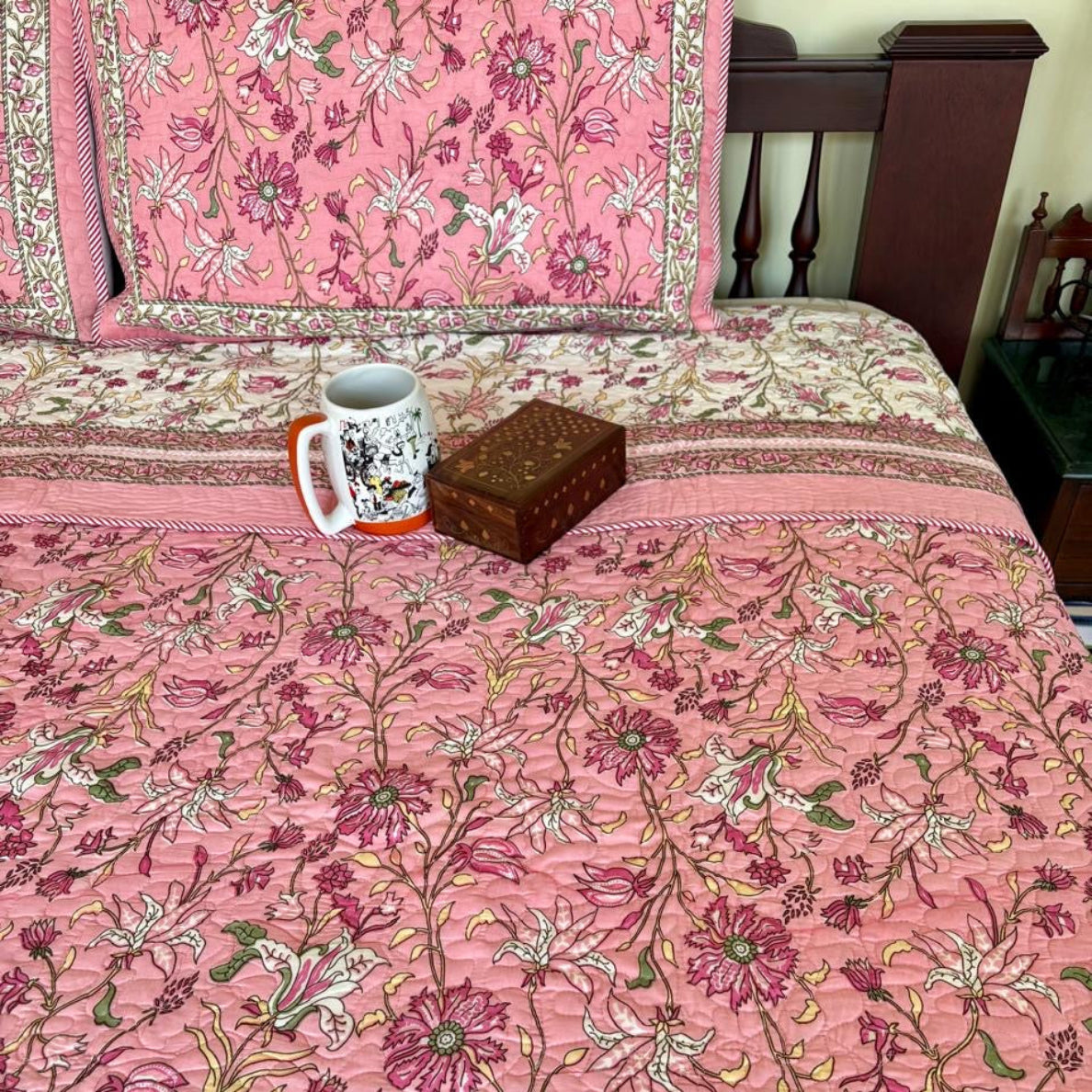Pink floral bedspread with a mug and box on a bed