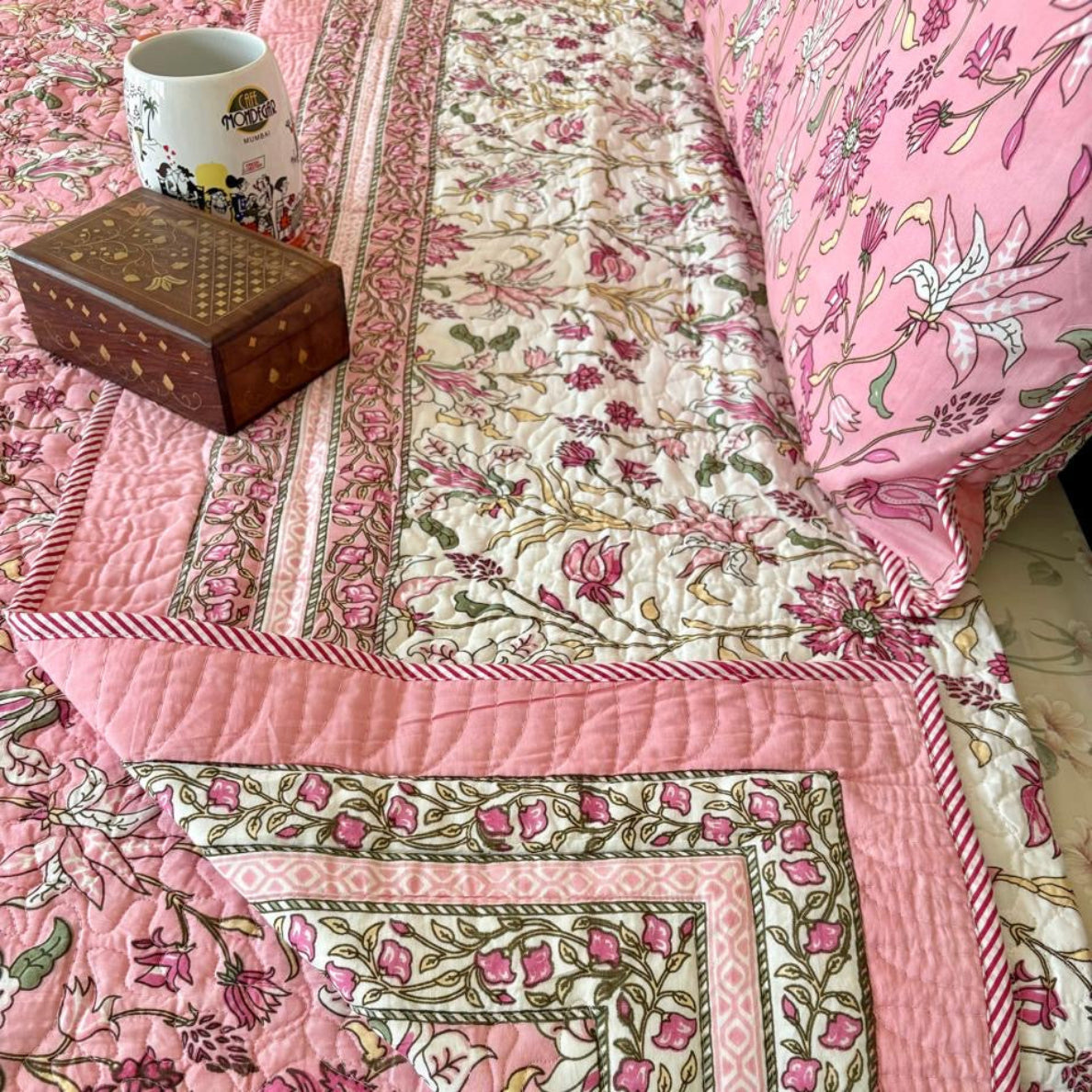 Floral patterned quilt with pink and green colors on a bed.