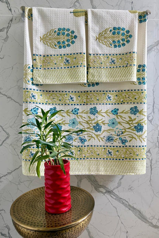 Decorative bath mat with floral pattern on a marble surface, accompanied by a plant in a red vase.