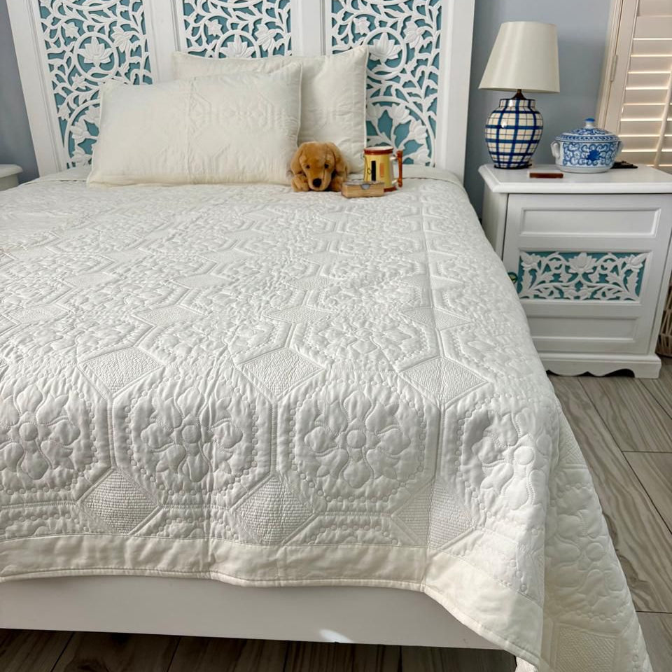 Bedroom with a white quilted cover on a bed, decorative headboard, and nightstand.