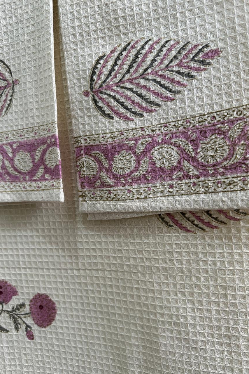 Set of folded fabric napkins with floral and leaf patterns on a textured surface.