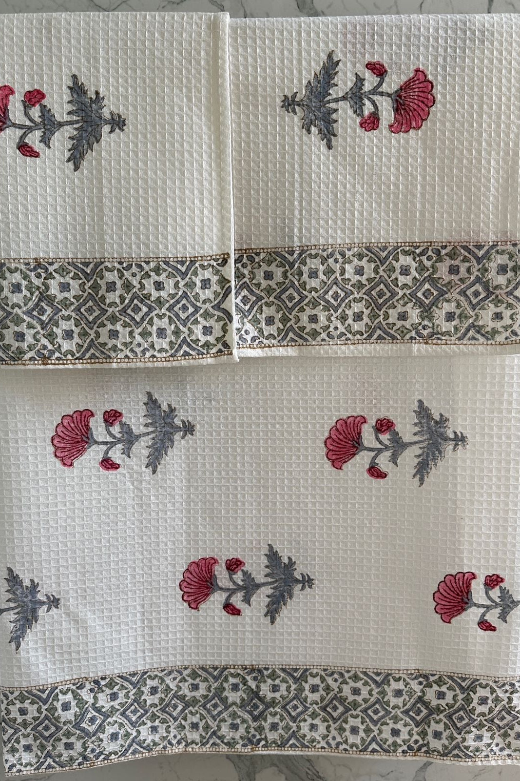 Set of three white towels with floral patterns on a gray surface