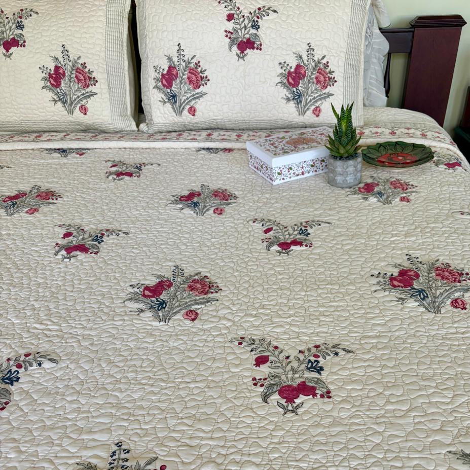 Floral patterned quilt on a bed with pillows and a plant in the background.
