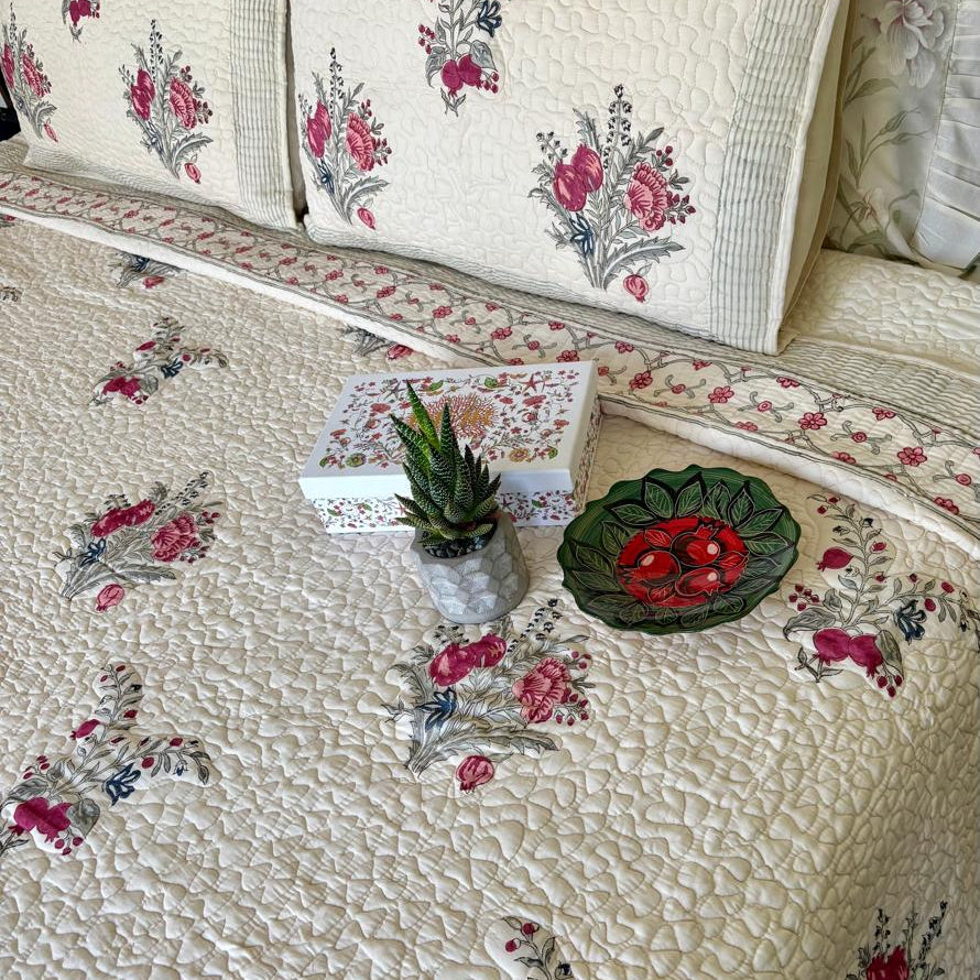 Floral patterned quilt with decorative pillows and a small plant on a bed.