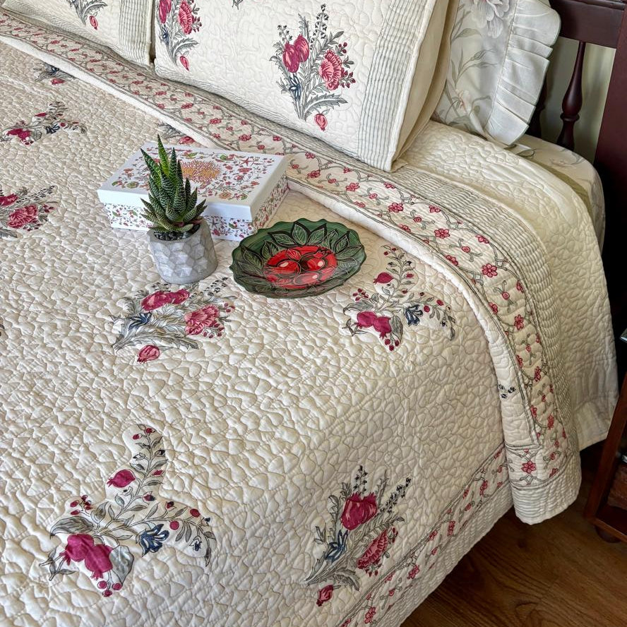 Floral patterned quilt on a bed with decorative items on a wooden floor.