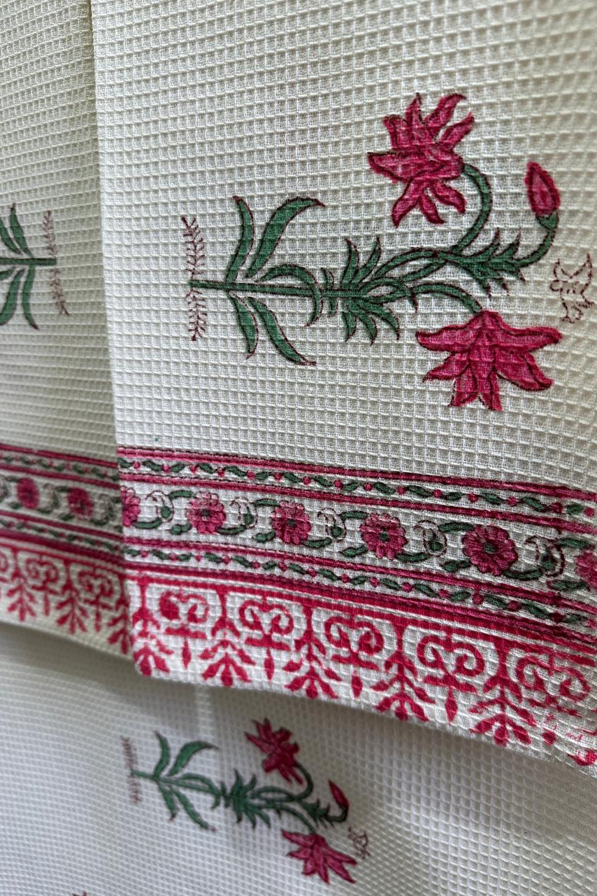 Close-up of a white waffle-weave fabric napkin or kitchen towel featuring embroidered pink flowers and green leaves, with a decorative pink and green border.