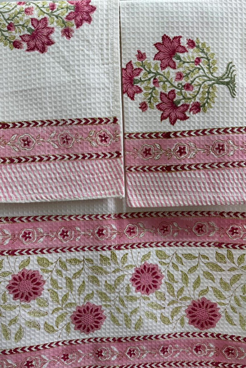Three white waffle-weave kitchen towels with pink floral embroidery and decorative pink borders, arranged together.