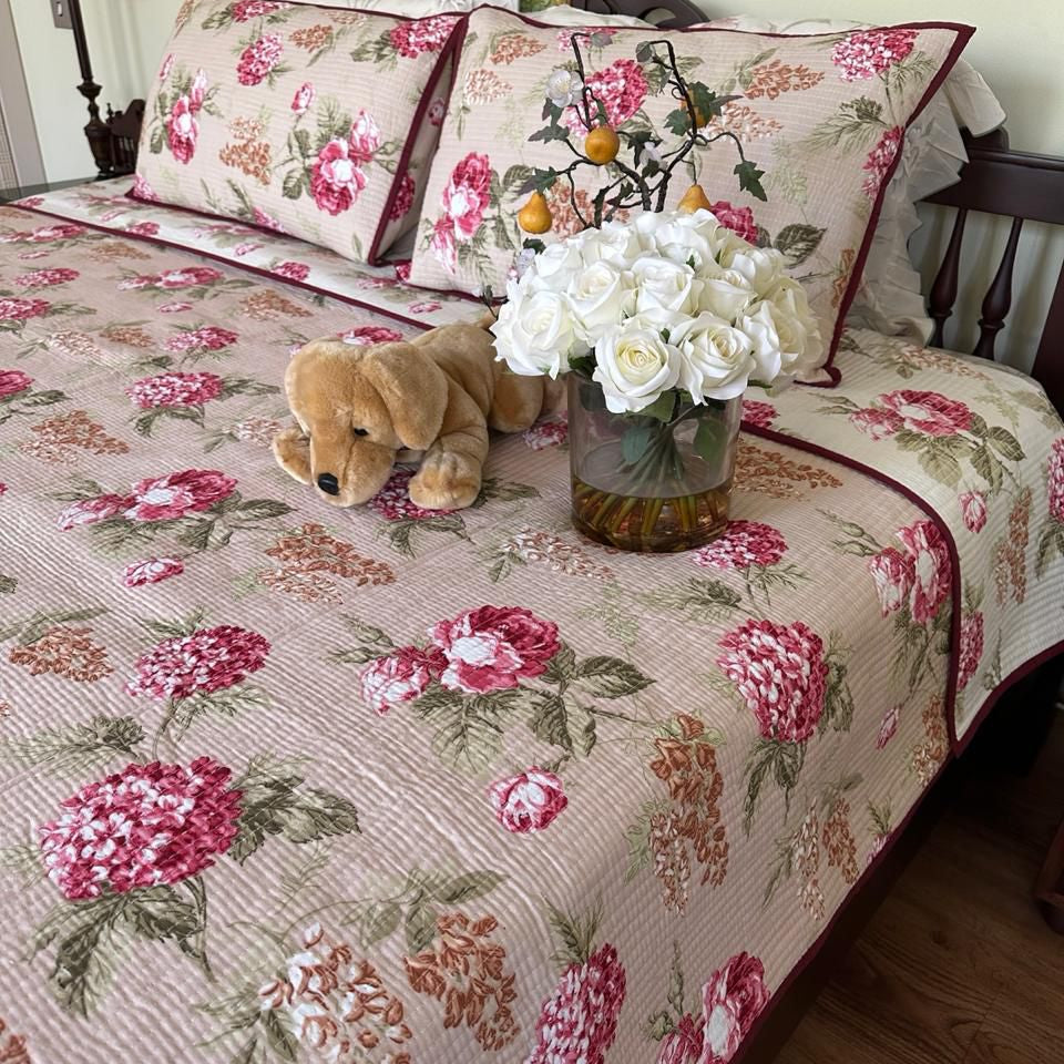 Floral patterned bedspread on a bed with a teddy bear and flowers.