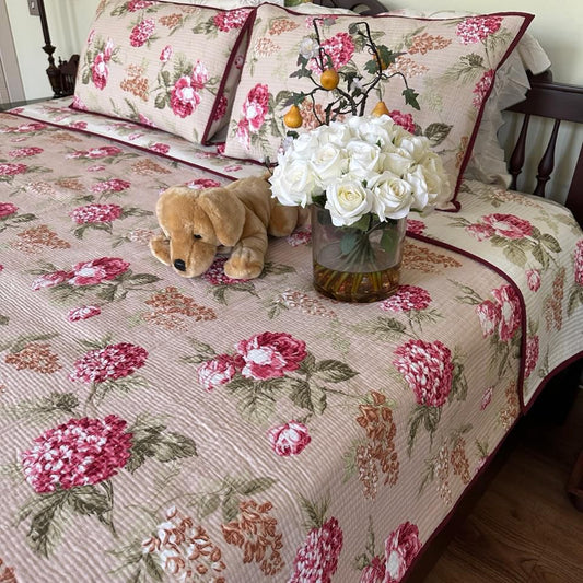 Floral patterned bedspread on a bed with a teddy bear and flowers.