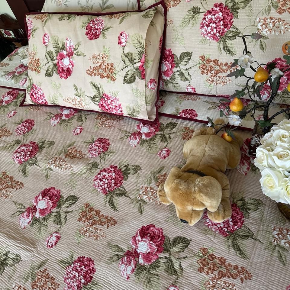 Floral patterned bedspread with pillows and a teddy bear on a bed.