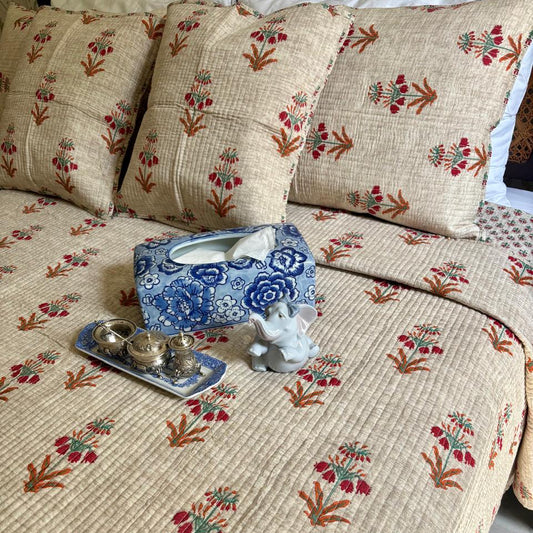 Floral-patterned bedspread with a tissue box and small tray on a bed.