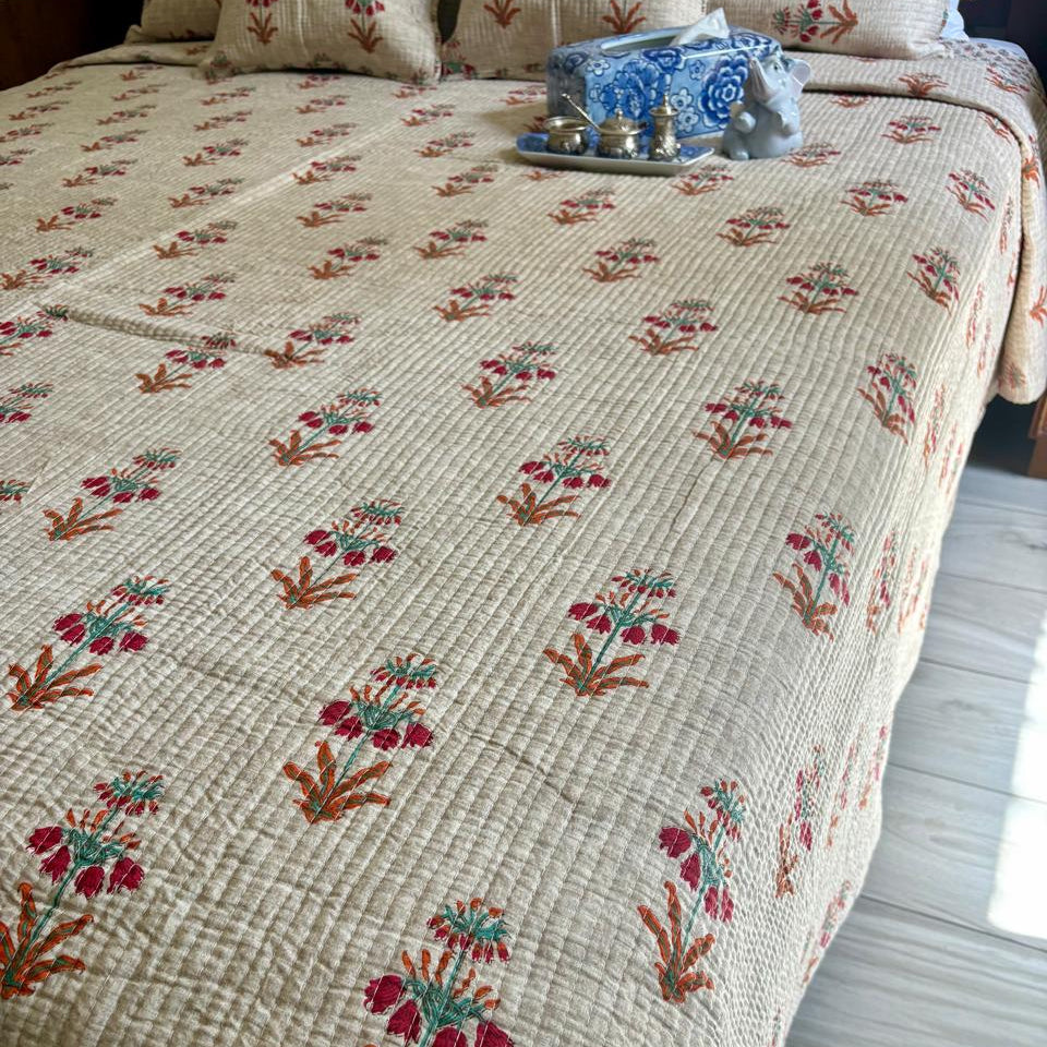 Floral patterned quilt on a bed with decorative items on a wooden floor.