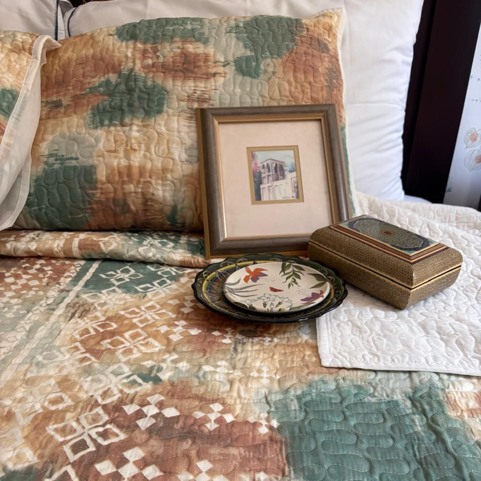 Decorative items including a framed picture, a small box, and a plate on a patterned fabric surface.