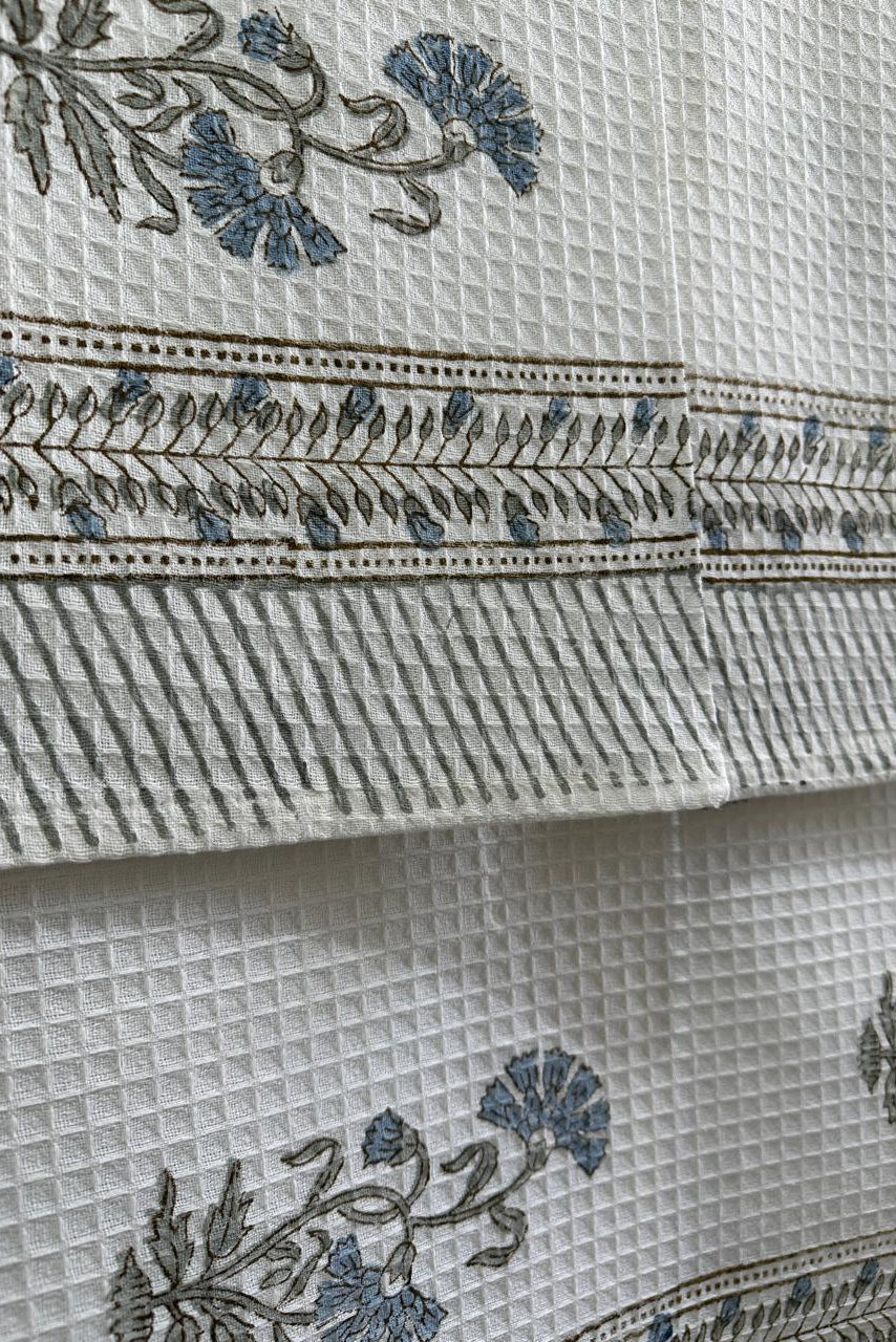 Close-up of a white textured fabric with blue floral embroidery and a decorative border pattern.