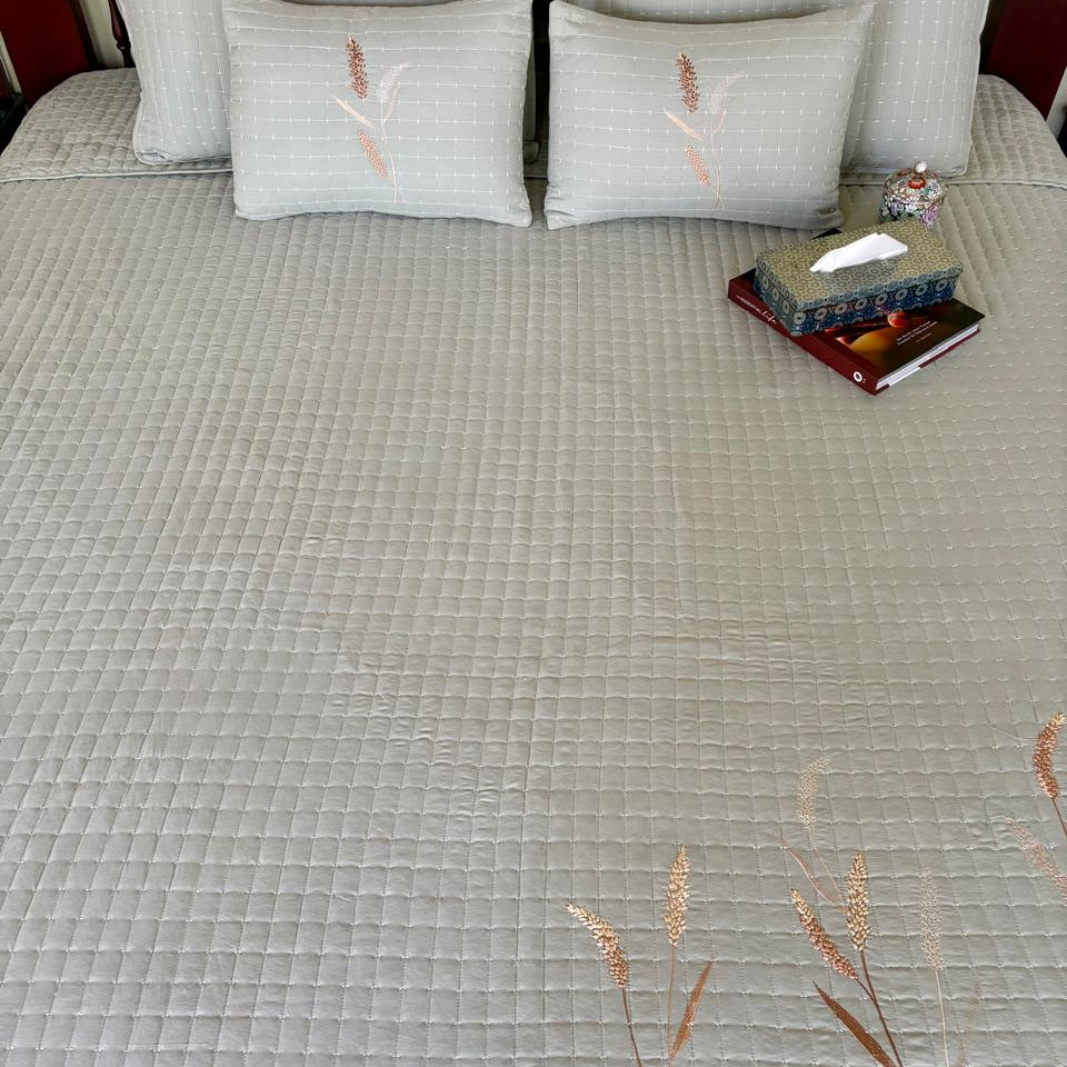Gray textured bedspread with floral patterns on a bed.