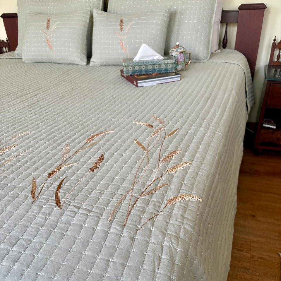 Quilted bedspread with floral embroidery on a bed in a bedroom setting.