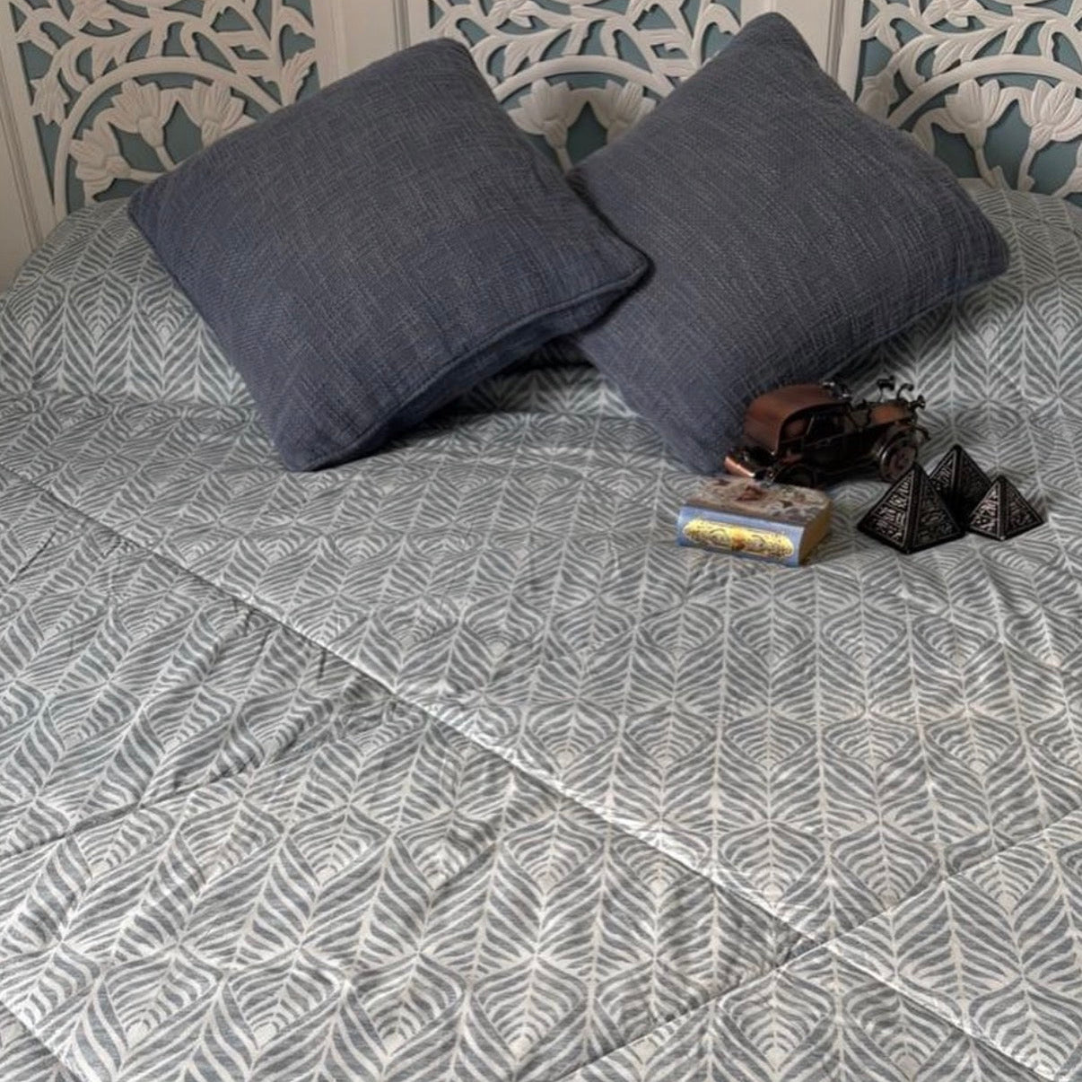 Gray patterned bedspread on a bed with decorative pillows and a headboard.